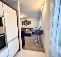A kitchen corner with appliances, bar seating, and a view of the living room in a 2-room apartment.