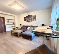 Living room in a two-room apartment with a sofa, decorations, and a wooden-patterned floor.