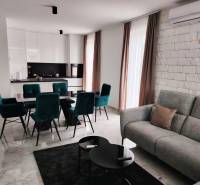 Living room with kitchen in a family house; marble floor, white cabinets, green chairs.