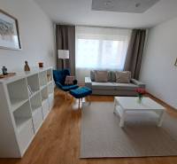 Living room in a three-room apartment with a wooden decor floor, a blue armchair, and white furniture.