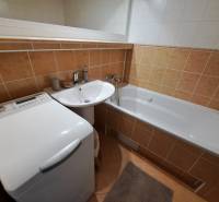 A bathroom in a 3-room apartment with a bathtub, sink, and washing machine, tiled with orange tiles.