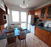 A kitchen in a 3-room apartment with a dining table, appliances, and cabinets with a wooden decor.