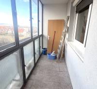 Glazed balcony of a 3-room apartment with tiles, a view of the surroundings, and stored tools.
