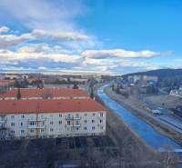 View of the town of Svit with a river, apartment buildings, and a forest in the distance.