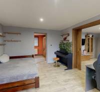 A room in a family house with a piano, a bed, and a wooden-patterned floor.