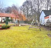 The garden of a family house in Unín with a wooden swing, bench, and hedge.