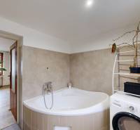 A bathroom in a family house with a corner bathtub, a washing machine, and flowers.
