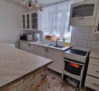 A kitchen in a family house with white cabinets, appliances, and a curtain on the window.