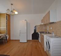 A kitchen in a studio apartment with a wood-patterned floor, a dining table, and appliances.