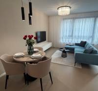 Living room in a two-room apartment with a gray sofa, dining table, and wooden decor flooring.
