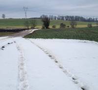 A snowy country road leading through residential plots near Seňa.