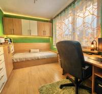 A room in a 4-room apartment with a desk, a bed, and a floor with a wood decor.