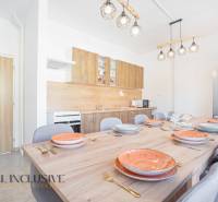 A kitchen with a large table, chairs, lights, and a kitchen unit with a wooden decor.