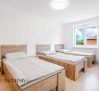 Three beds in a room with a wooden floor and a large window.