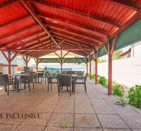 A gazebo in Dunajská Streda with a wooden roof, chairs, and tables on a concrete surface.