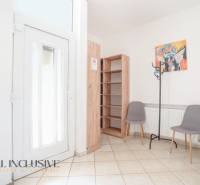 Interior of a building with entrance doors, tiles, a shelf, two chairs, and a coat rack.