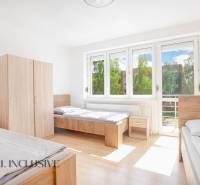 A bright room with three beds, white walls, wardrobes, and large windows.