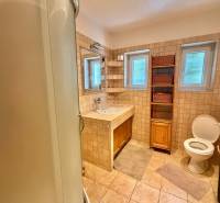 A bathroom in a family house with ceramic tiles, a shower enclosure, and storage space.