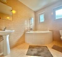 A bathroom in a family house with a bathtub, sink, and toilet, tiled with light tiles.