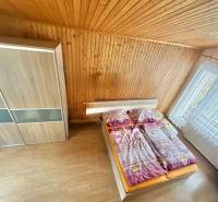 Bedroom in a family house with wooden paneling, wood-patterned floor, large window.