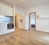 A kitchen in a studio apartment with white cabinets and a wooden decor floor.