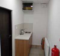 A narrow office kitchenette with a sink, fire alarm, and white walls.