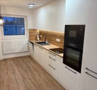 A kitchen in a 3-room apartment with white cabinets, wood-patterned flooring, and a built-in oven.