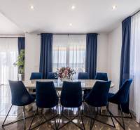 Dining room in the villa with dark curtains, wood-patterned flooring, and blue chairs.
