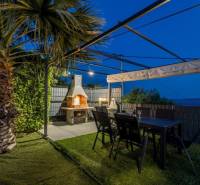 The palm garden of the villa in Kaštela with a pergola, fireplace, and table.