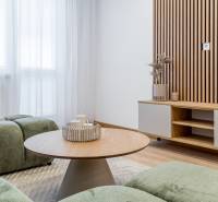 Living room in a two-room apartment, wooden decor, green sofas, round table, light curtains.