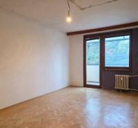A vacant room in a 2-room apartment with a wooden decor floor and a window to the balcony.