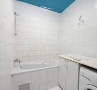 Bathroom in a 2-room apartment with a bathtub, white tiles, and a washing machine.