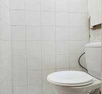 A toilet in a 2-room apartment with white tiles and flooring.