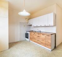 A kitchen of a two-room apartment with white cabinets and a wooden decor floor.