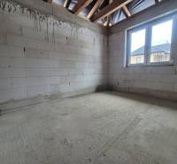 Concrete floor, unpainted bricks, and wooden beams in the interior of a family house.