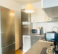 A kitchen in a 2-room apartment with a cooktop, microwave, and a floor with a wooden decor.