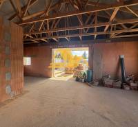 Unfinished interior of a family house with exposed wooden ceiling beams and raw bricks.