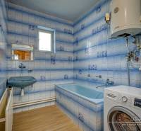 A bathroom with a shower and a washing machine in a family house. Blue tiles and a white boiler.
