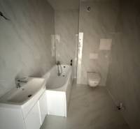 Bathroom in a 2-room apartment with a bathtub and a sink, tiled with light ceramics.