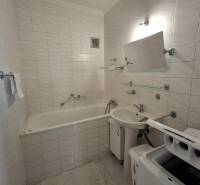 A bathroom with a bathtub and a washing machine in a 3-room apartment, tiled with light tiles.