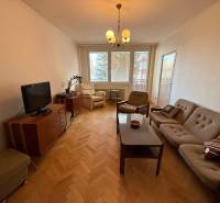 Living room in a three-room apartment with a sofa, television, and wooden decor flooring.