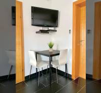 A dining room in a family house with a corner table, a TV on the wall, and black tiles.