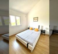 Bedroom in a family house with a wood-patterned floor, a bed, and a window.