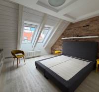 Bright attic bedroom with a double bed and wood-patterned flooring.