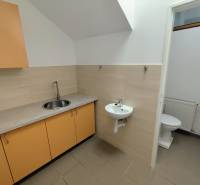 A sink, cabinets, and a toilet in commercial premises with light tiles on the wall.