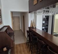 A bar counter with stools in a studio apartment, next to a hallway with wooden doors.
