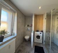 A bathroom in a 2-room apartment with a washing machine, shower, and window.
