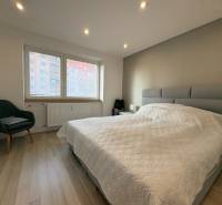 A bedroom in a 2-room apartment with a wood-patterned floor, a comfortable armchair, and a large window.