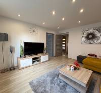 Living room in a two-room apartment with a wooden decor floor, TV, and yellow sofa.