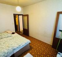 A bedroom with a carpet, a bed, and light-colored walls in a 2-room apartment.